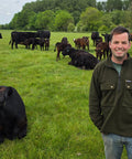 Man standing in a field with cows under a blue sky with clouds.